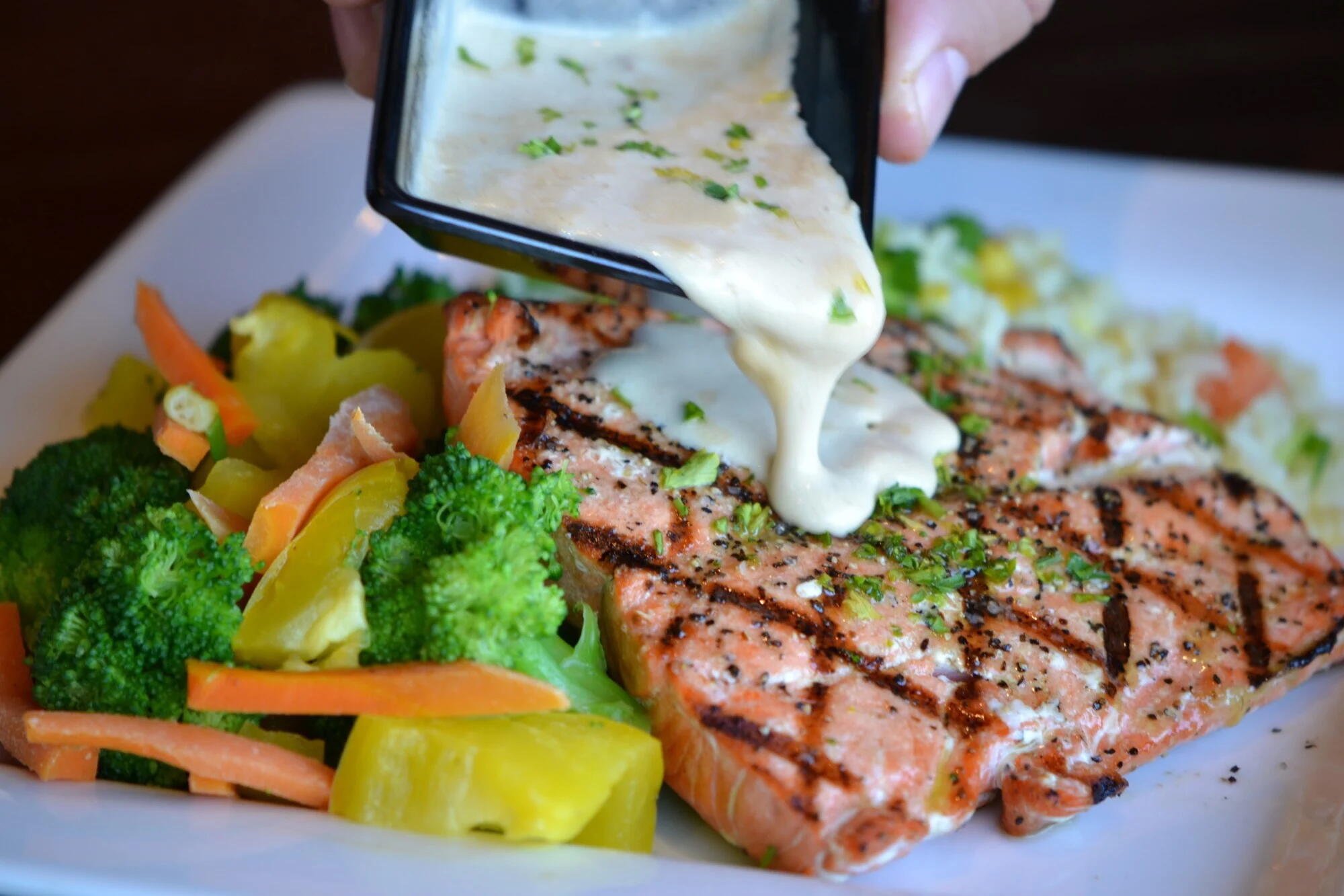 sauce pouring over steak with a side of vegetables